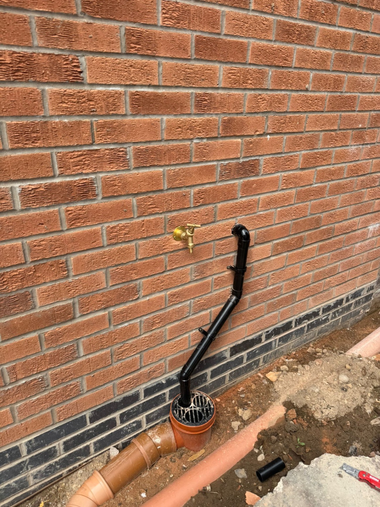 External brass garden tap and new black soil pipe connection to gully on brick wall