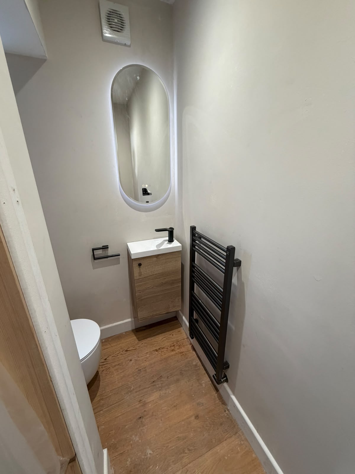 Downstairs cupboard converted to a cloakroom WC with wall-hung toilet, oak vanity basin, LED oval mirror and black heated towel rail, Coventry