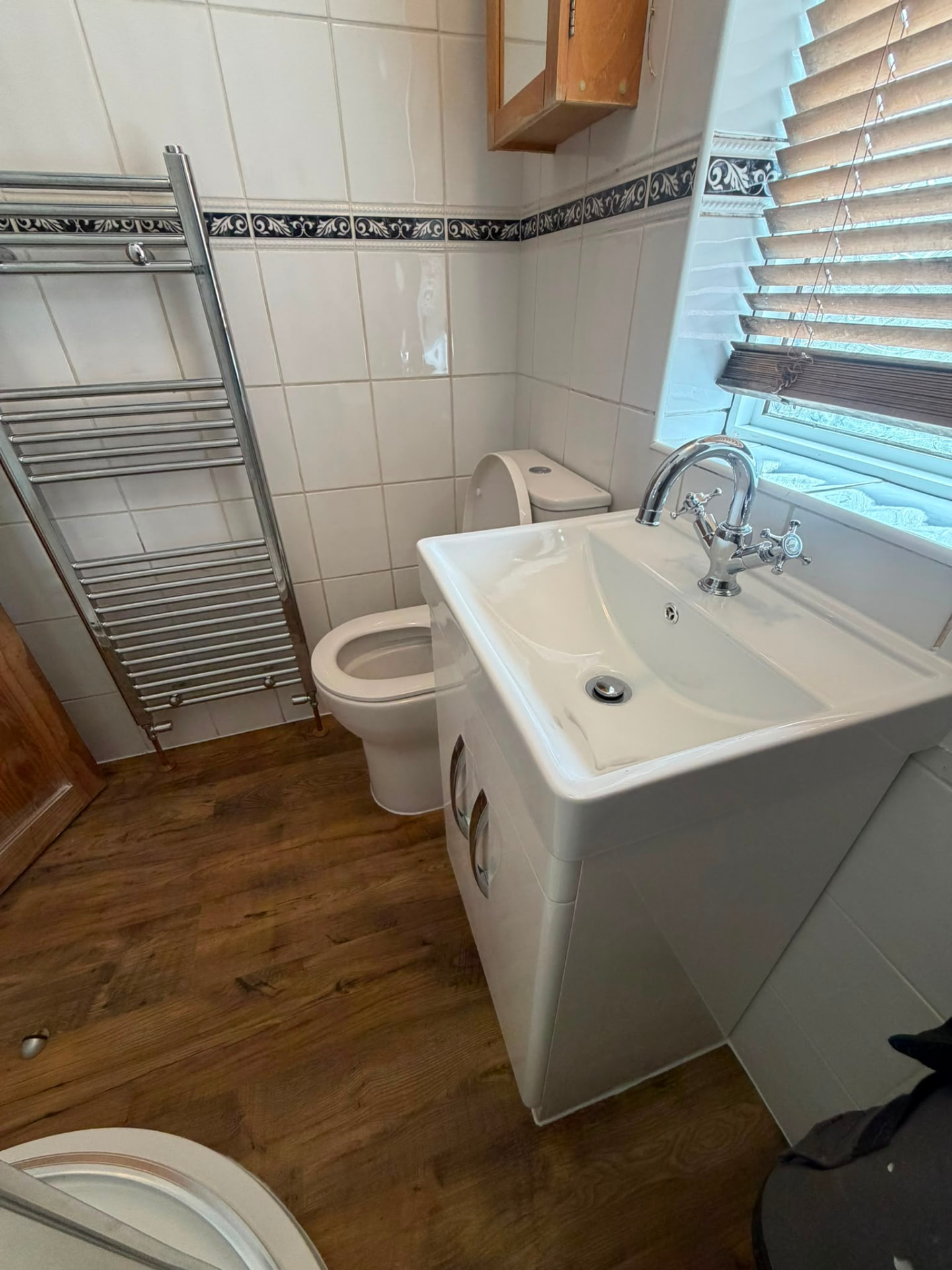 Cloakroom refit with chrome ladder heated towel rail, back-to-wall toilet and vanity basin on wood-effect flooring
