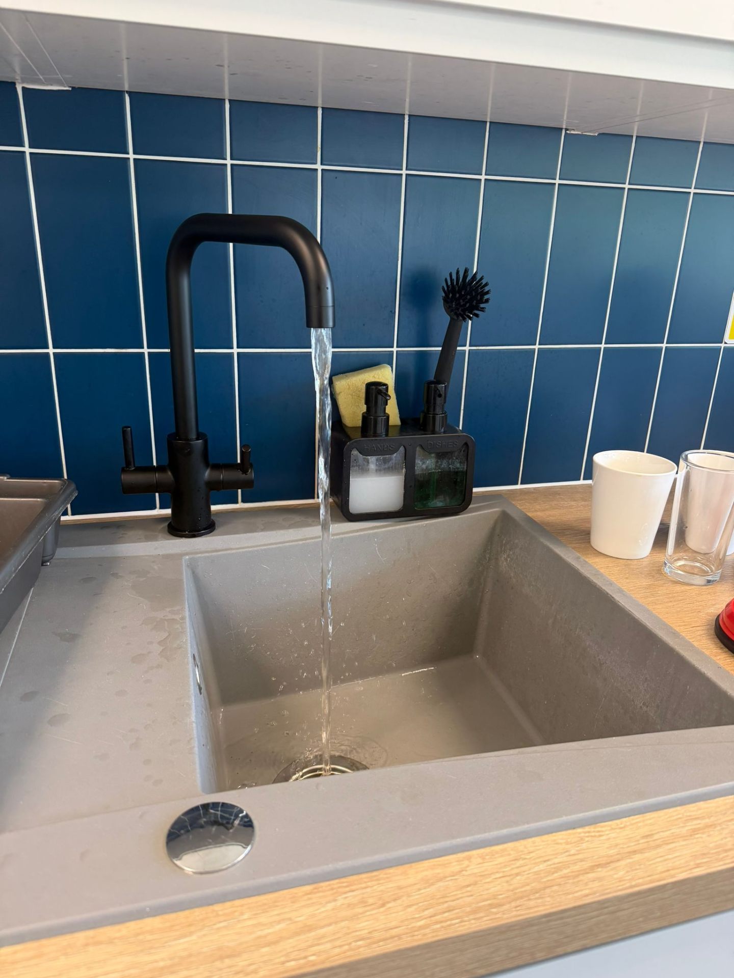 Undermount grey composite kitchen sink with matte black mixer tap and blue metro tiled splashback